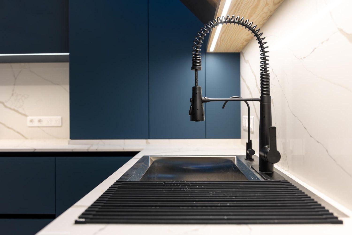 Schwarze Küchenarmatur mit Federhals über schwarzem Spülbecken in moderner Küche mit blauen Schränken und weißer Arbeitsplatte.